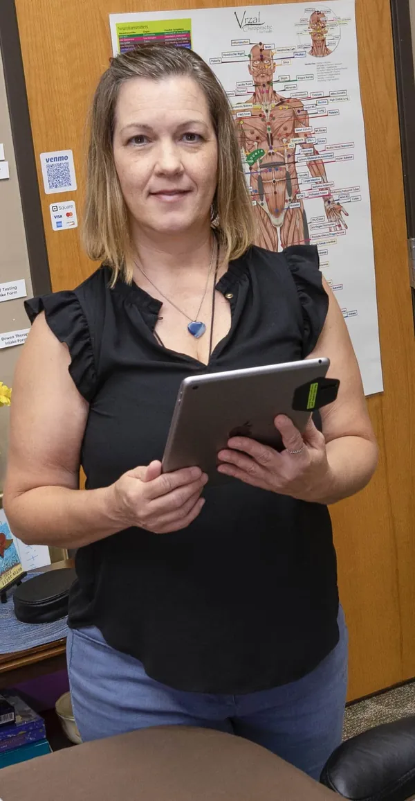 Jennifer Meyer-Kaiser in her Howell office, holding a tablet in front of a body-systems chart
